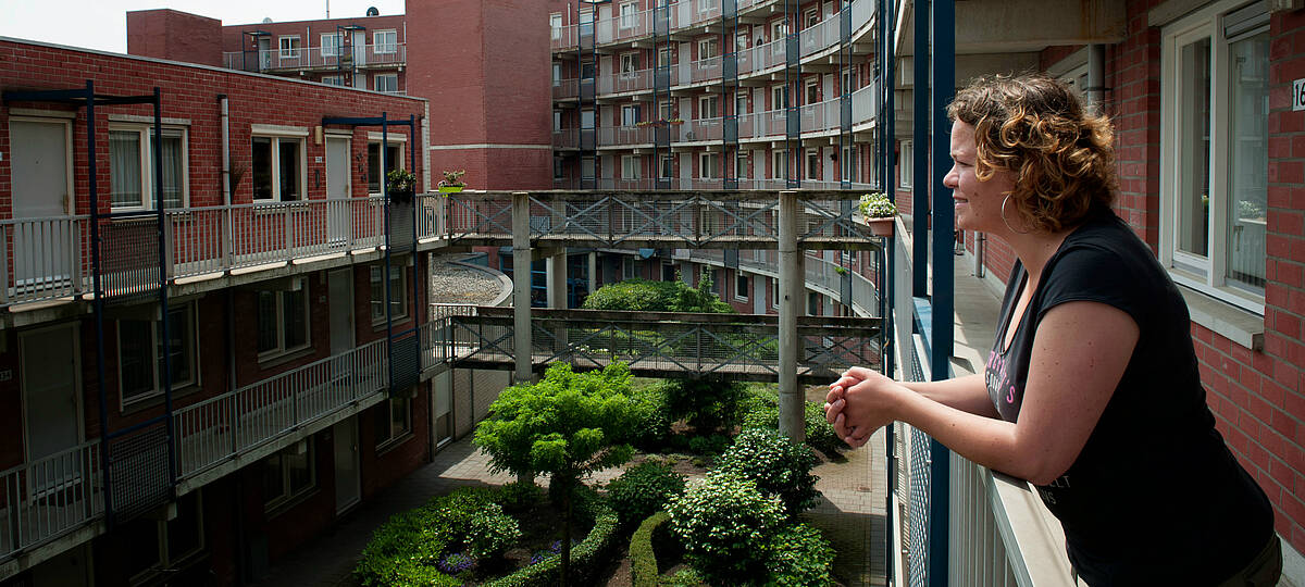 bewoonster kijkt vanaf haar balkon over de binnentuin van het wooncomplex
