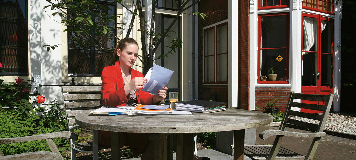 vrouw is in de tuin van haar woning in de zon aan het werk met mappen en post